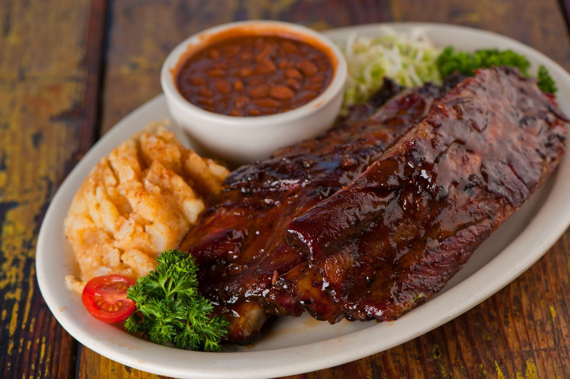 Plate of BBQ ribs with baked beans, mashed potatoes, and coleslaw.
