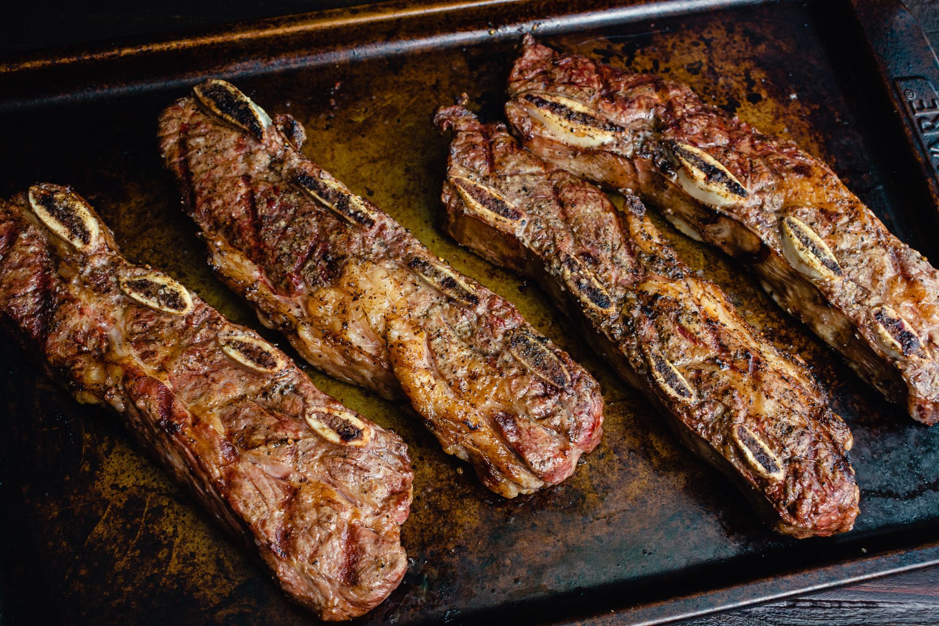 Roasted short ribs on a dark baking sheet, showing browned exterior and visible bones.