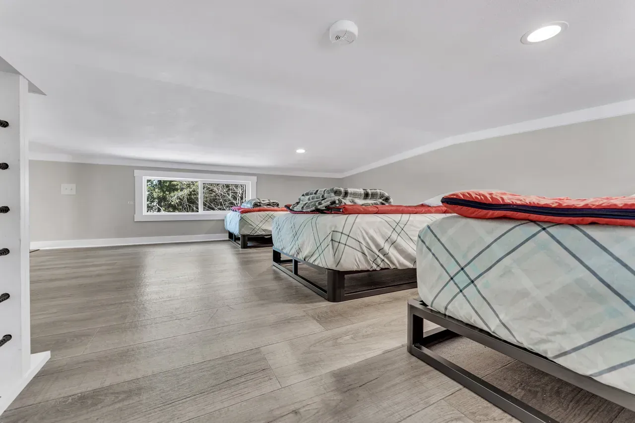 Loft bedroom with three beds, window, gray walls, and light wood flooring.