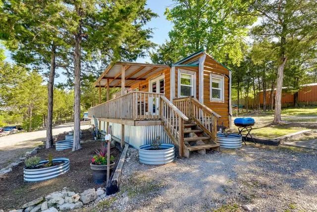 Small wooden cabin with porch, surrounded by trees and decorative planters.