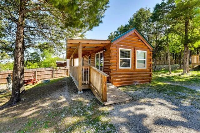 Small wooden cabin with a porch and ramp in a wooded area.