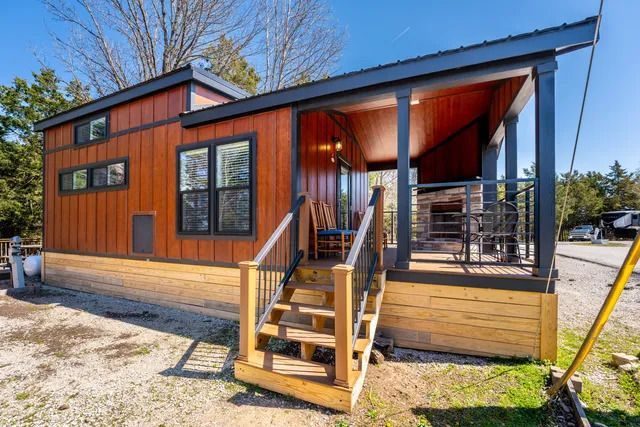 Tiny house with wooden facade and porch, black trim, and stairs.