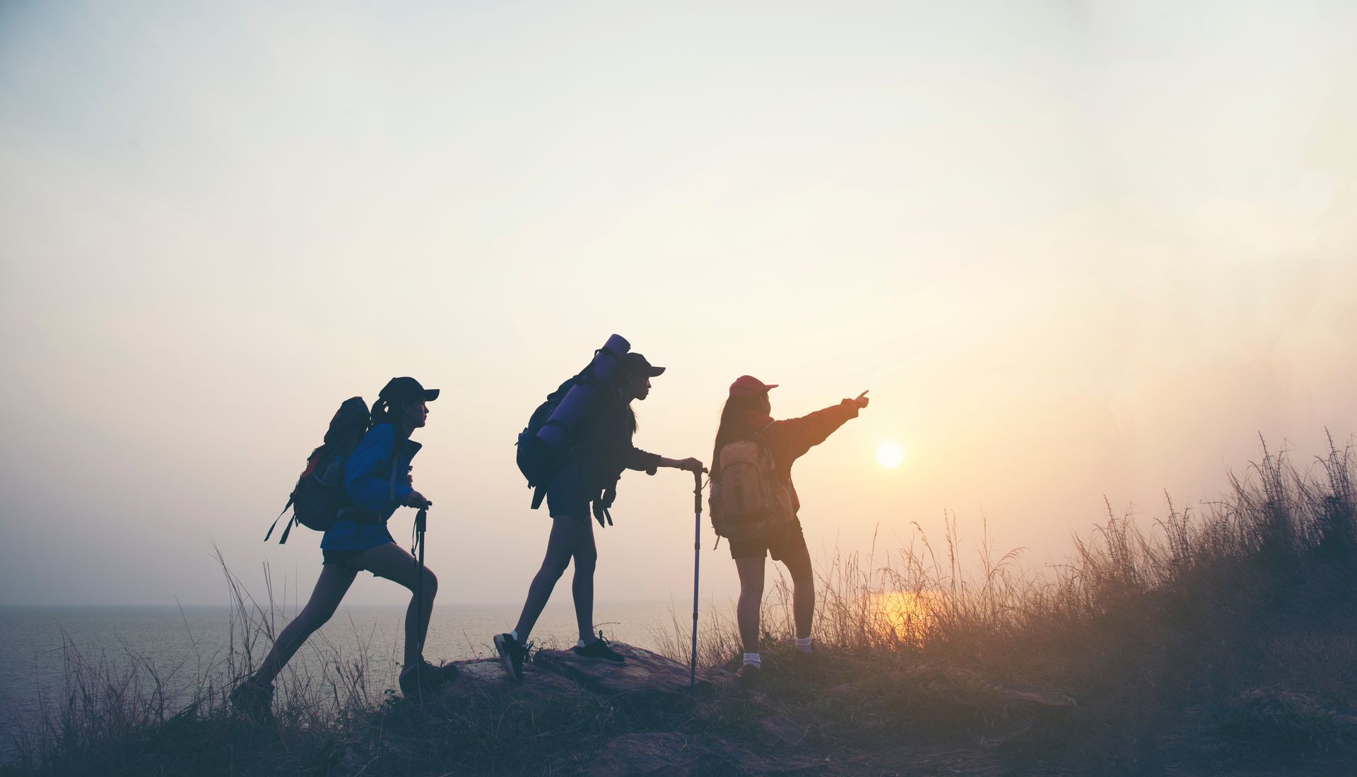 Silhouettes of people hiking against a sunrise.