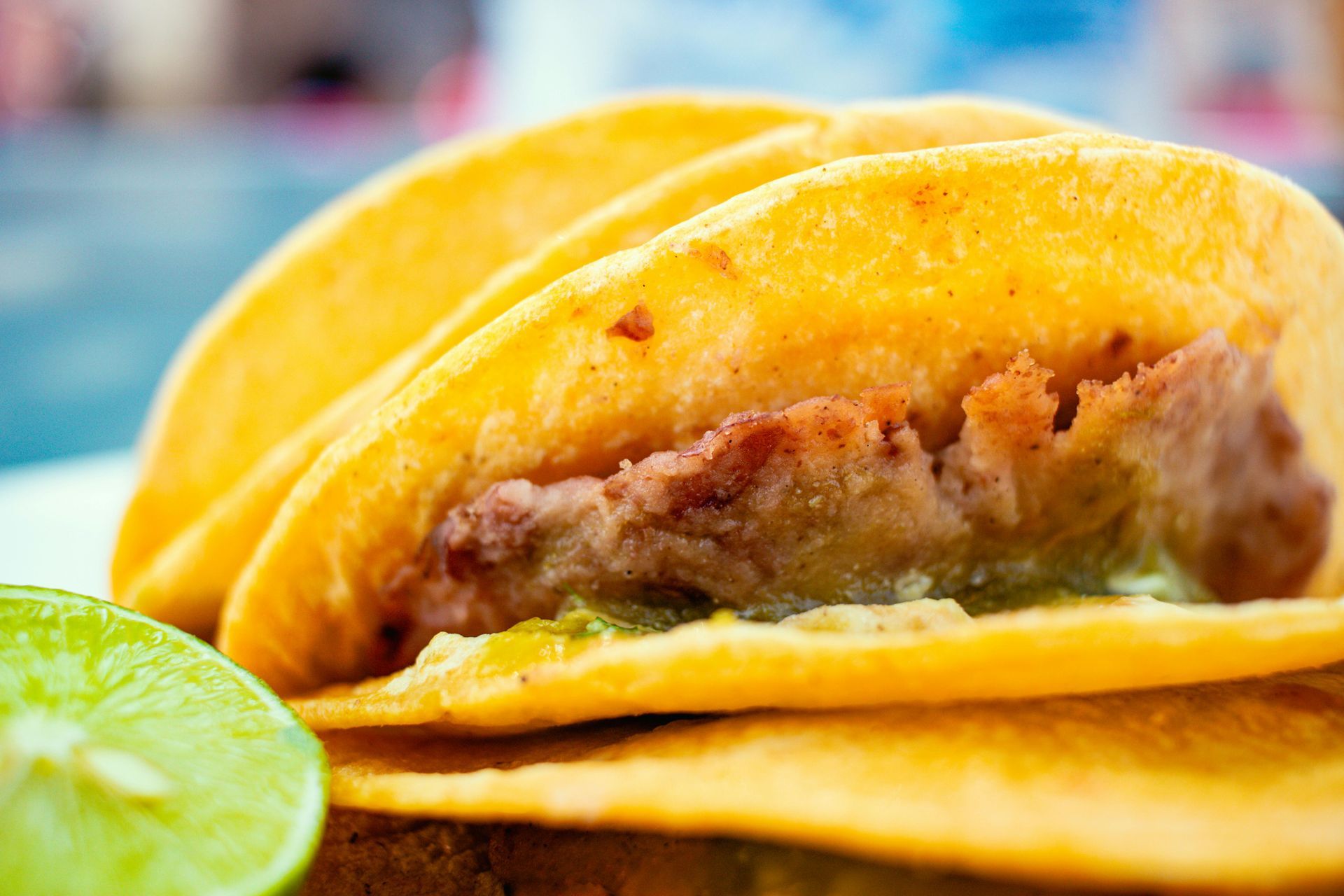 Three golden-fried tacos stacked with visible filling, a lime wedge in front.