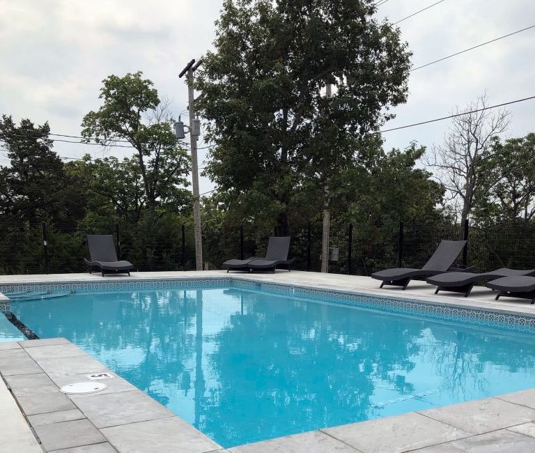 Swimming pool with several lounge chairs, surrounded by trees and a cloudy sky.
