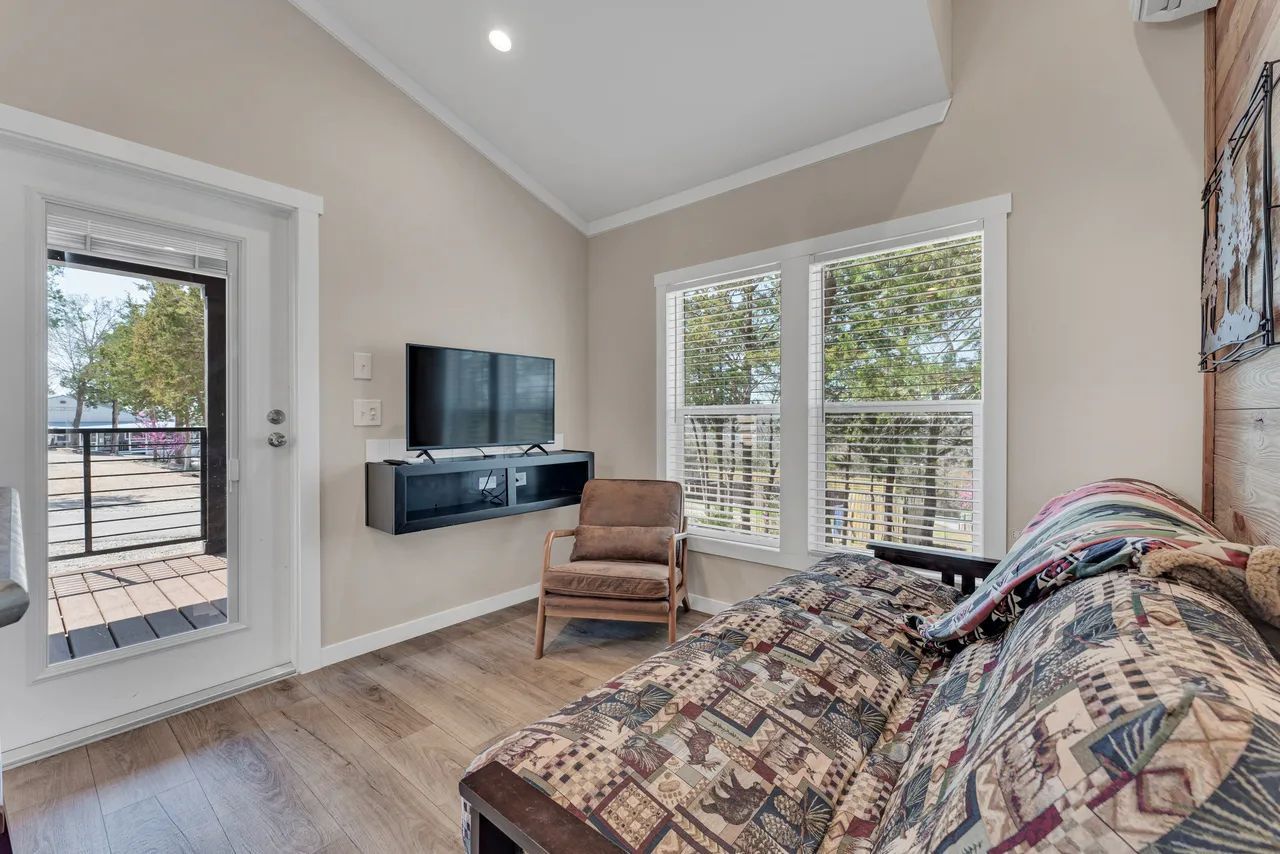 Cozy living room with sofa, TV, and door leading to a deck. Light walls and flooring.