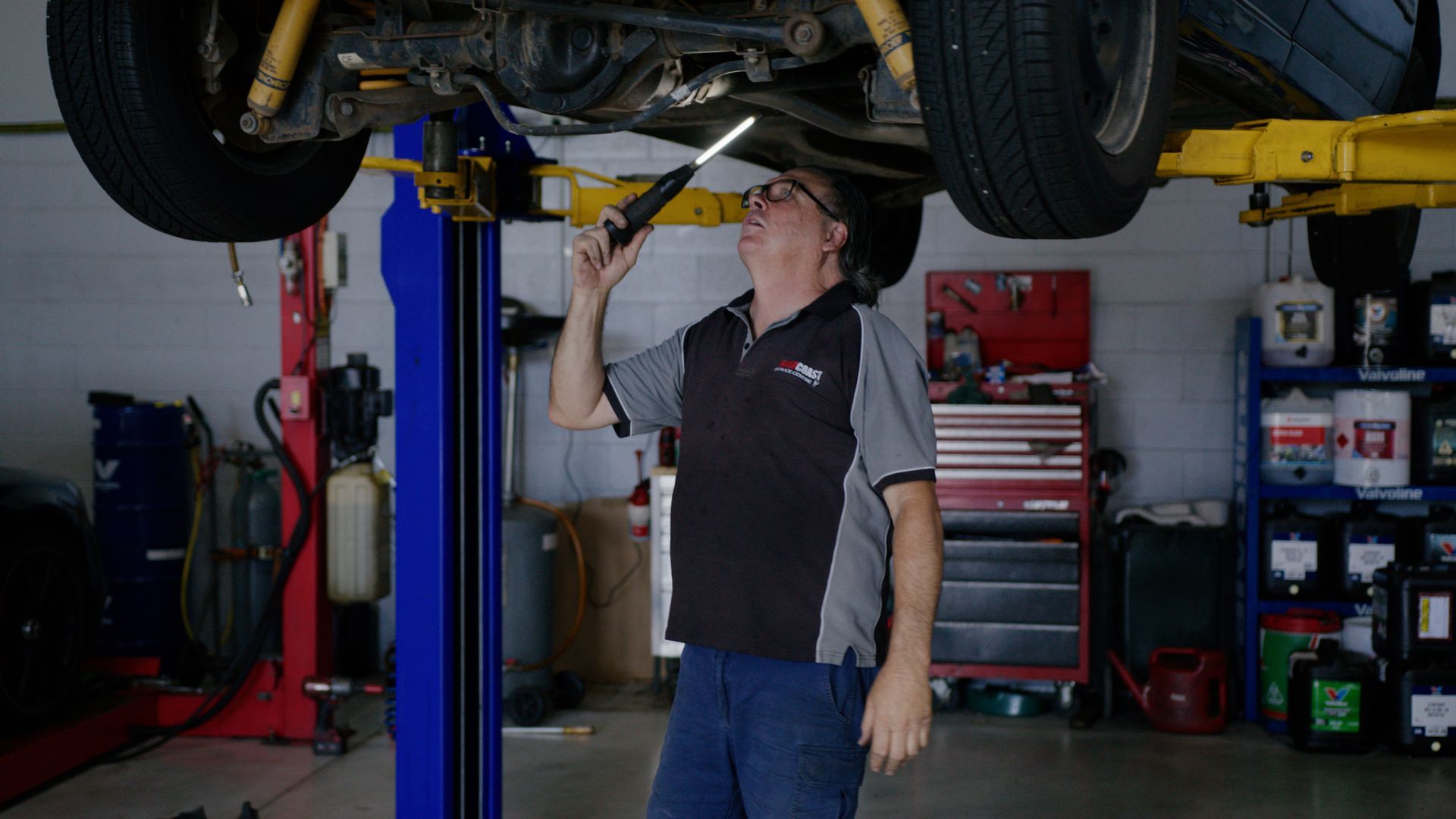 Mechanic inspecting underside of a car on a lift in an auto repair shop
