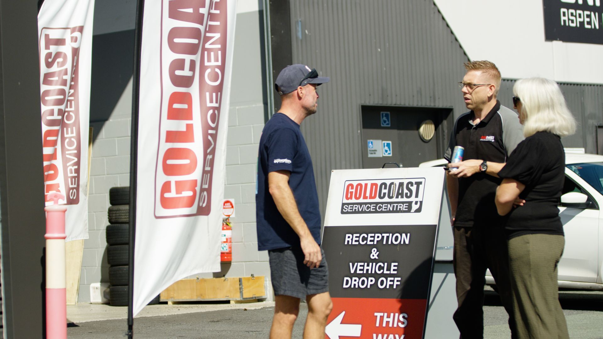 Two people talking outside a Gold Coast sales office with a promotional sign and banner.