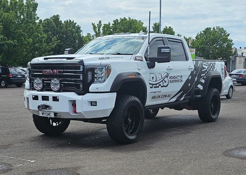 A mechanic in a blue uniform writes on a clipboard while standing next to a car with its hood open in a repair shop.