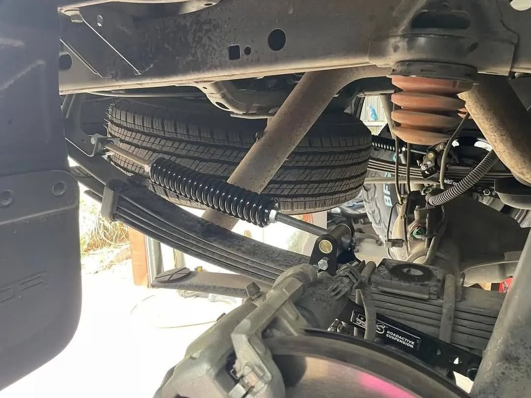 Four smiling people stand with arms crossed in front of a garage workshop, wearing matching navy work shirts.