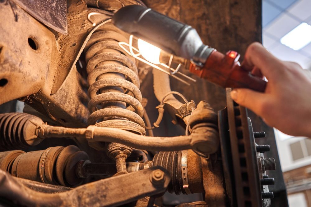 Four smiling people stand with arms crossed in front of a garage workshop, wearing matching navy work shirts.