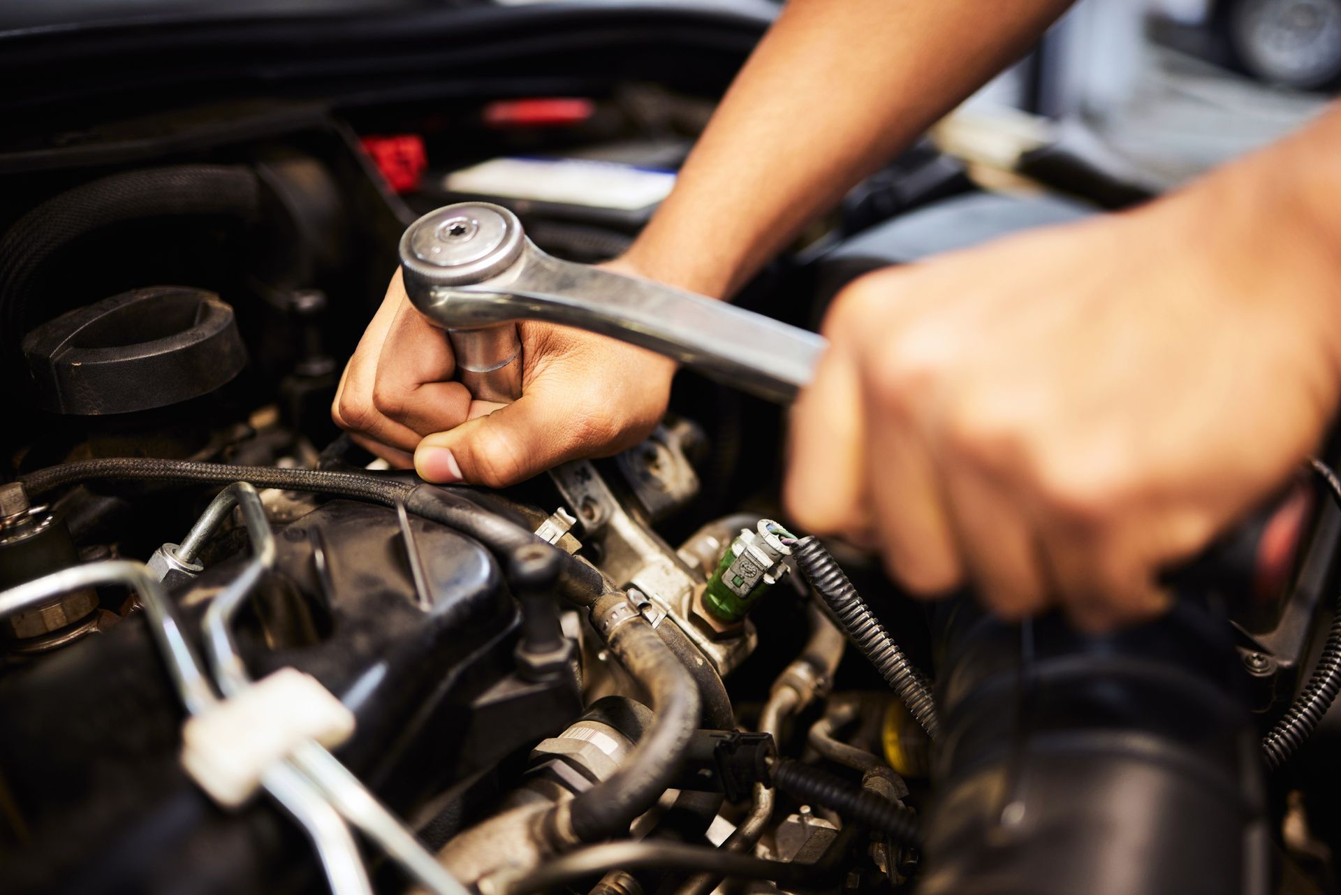 A close-up view of hands using a ratchet wrench to work on a car engine.