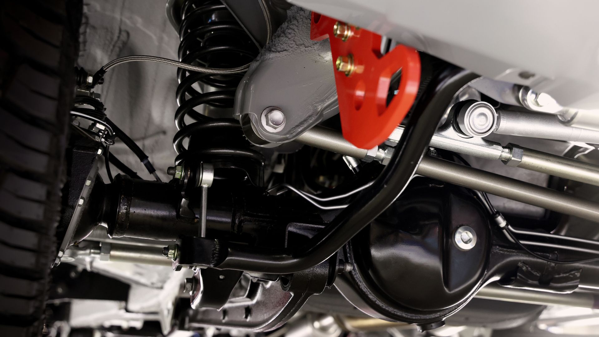 Close-up view of a vehicle's undercarriage showing suspension springs, a black axle, and a bright orange metal bracket.