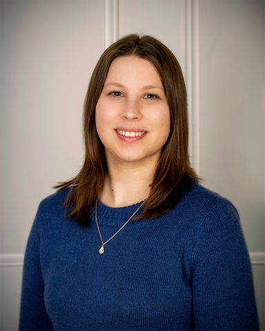 Portrait of a smiling woman in a blue sweater against a neutral gray background