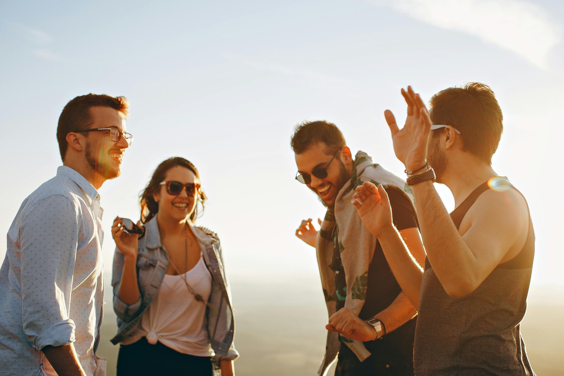 Four friends chatting and smiling outdoors in warm sunlight, one clapping