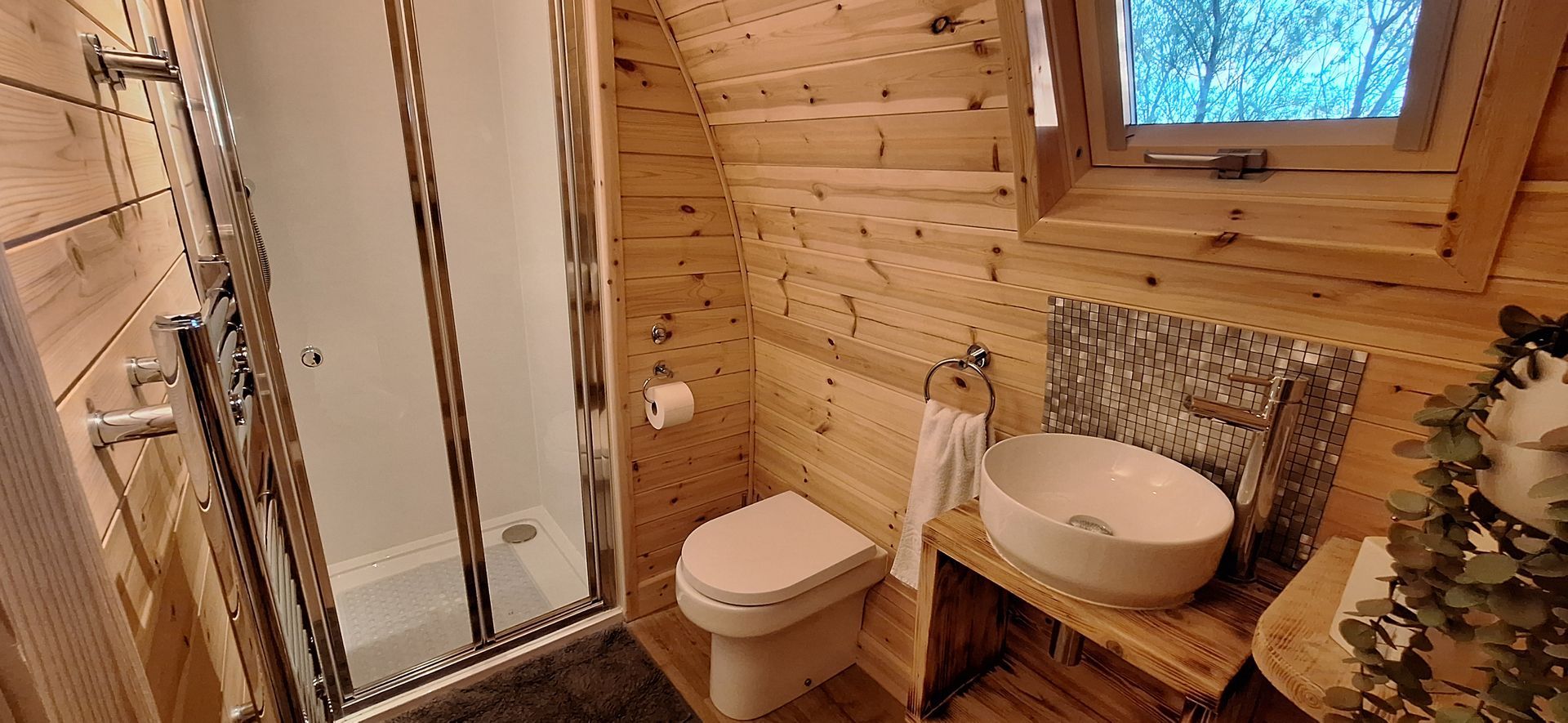 A bathroom in a log cabin with a toilet , sink and shower.