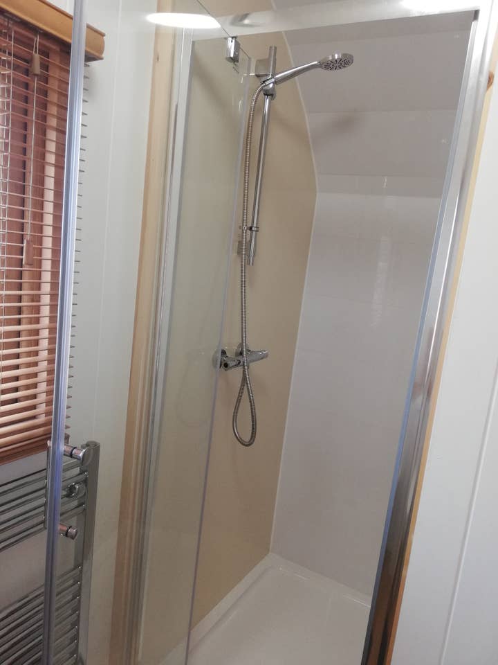 A bathroom with a shower and a window with blinds.