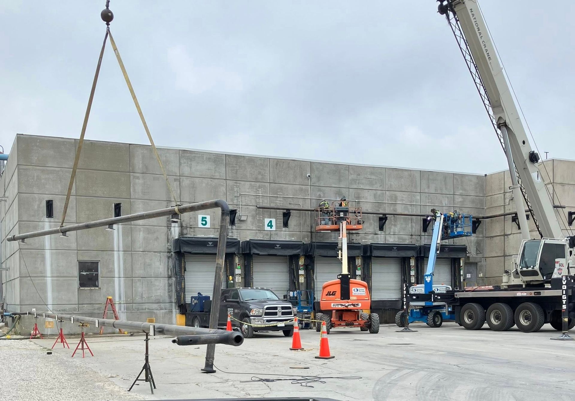 A crane is lifting a pipe in front of a building.