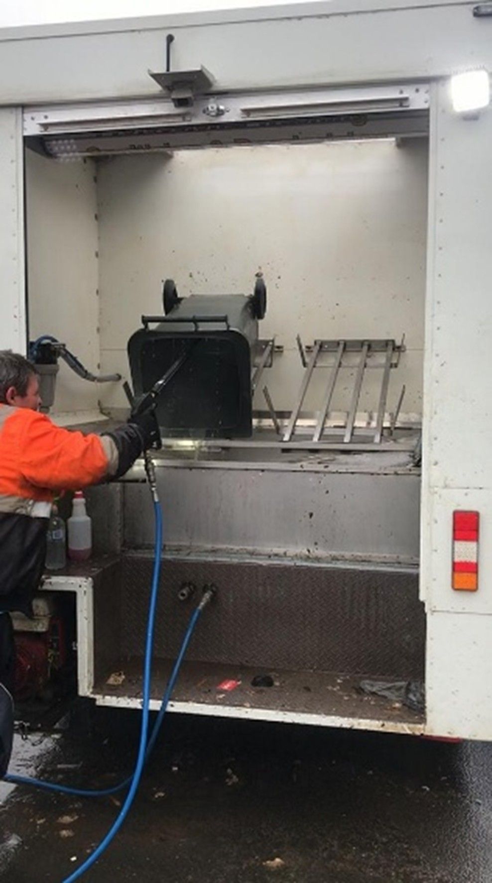 A worker is performing a bin cleaning service, using a high-pressure tool.