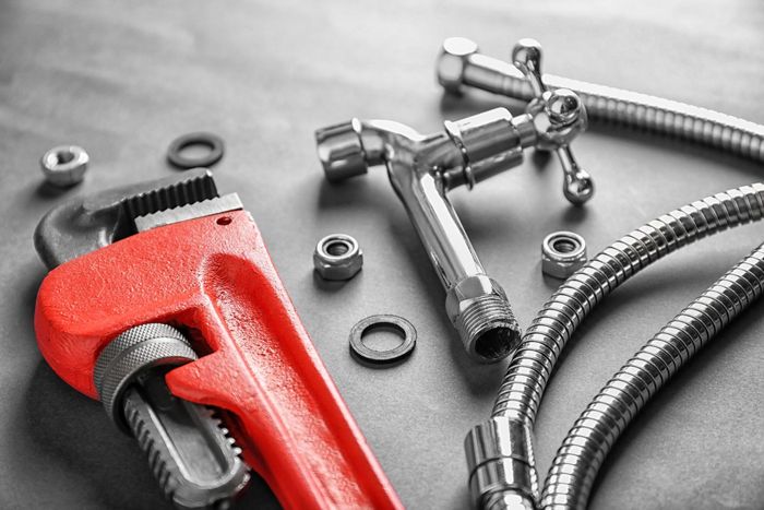 A close up of a wrench , hose , and faucet on a table.