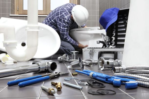 Plumber installing a toilet in a bathroom, surrounded by tools and plumbing parts.
