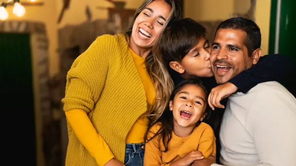 Smiling family cuddling on a couch, with a child leaning in between two adults.