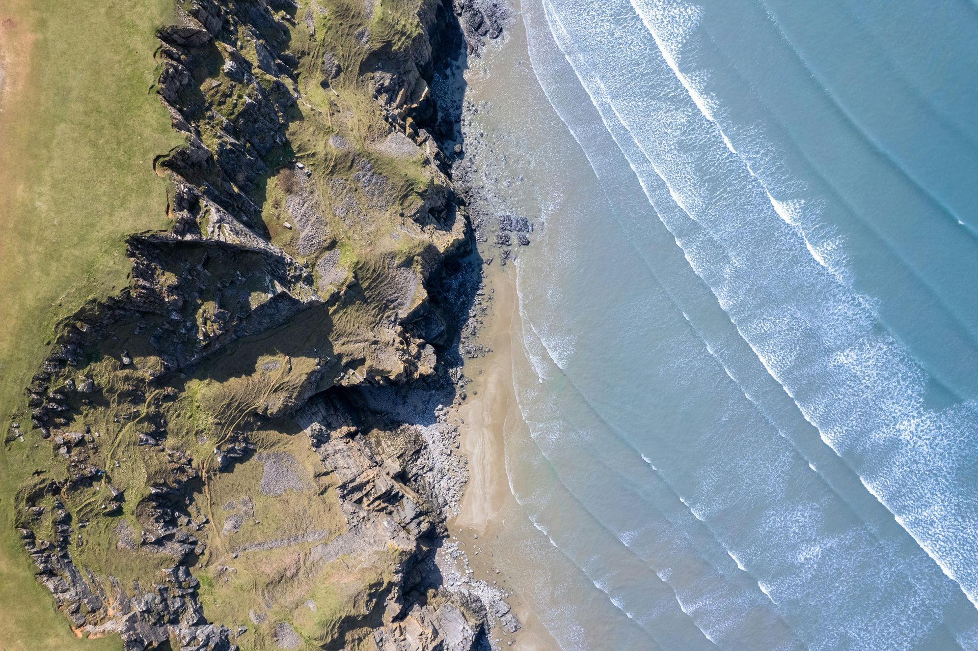 Aerial view of a rocky coastline meeting a sandy beach and ocean with gentle waves.