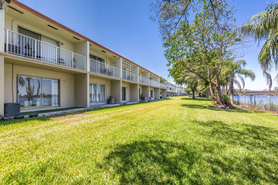 A row of apartment buildings with balconies and a large lawn in front of them.