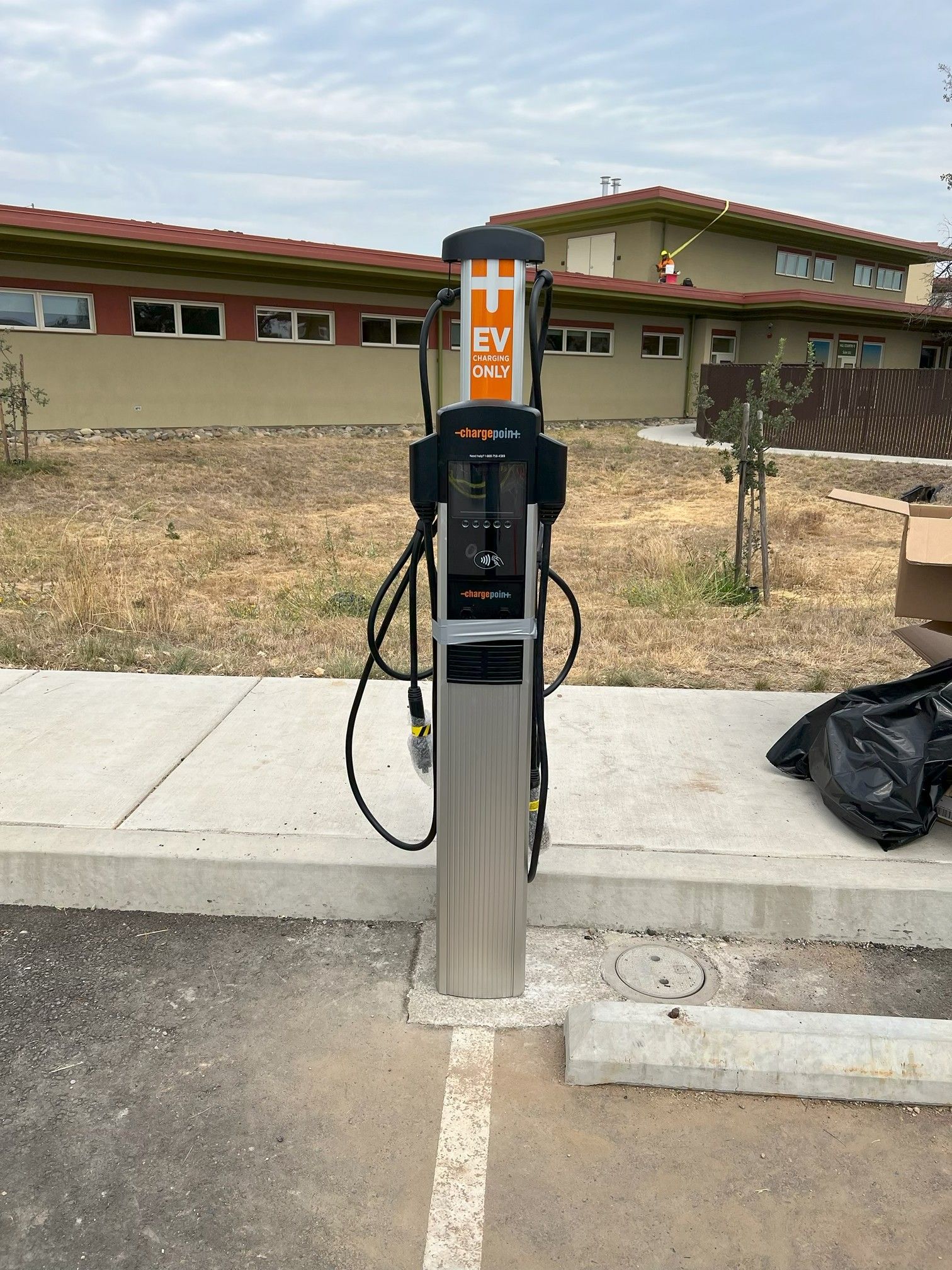 EV charging station on a sidewalk beside a building, with cables hanging from the unit.