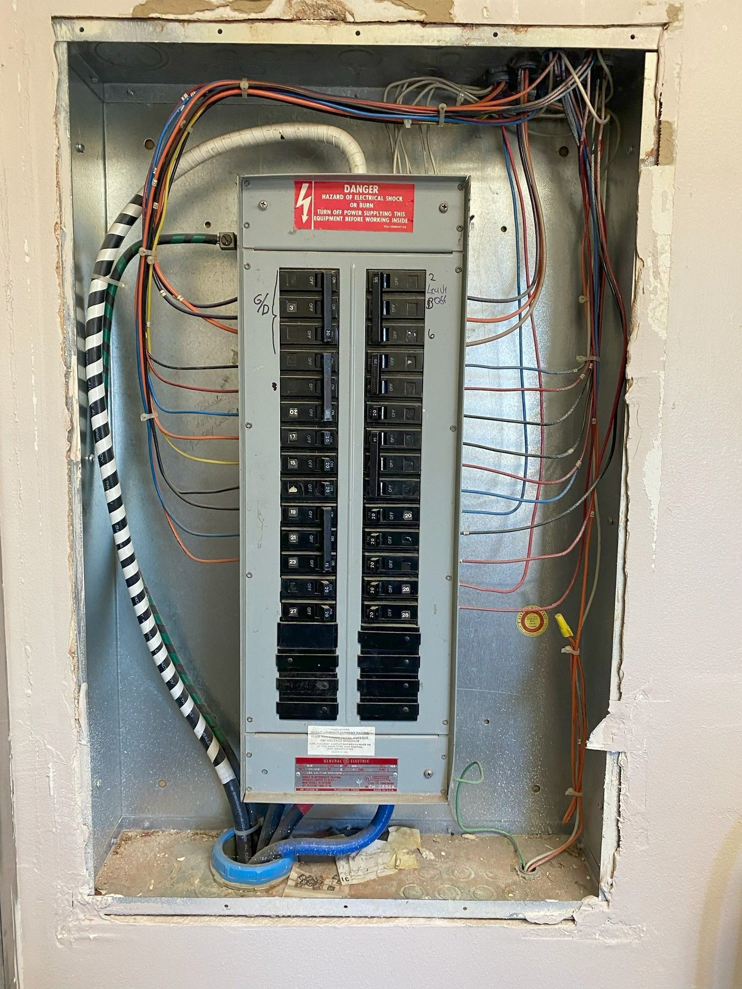 Open electrical breaker panel in a wall recess with exposed wiring and cables around it