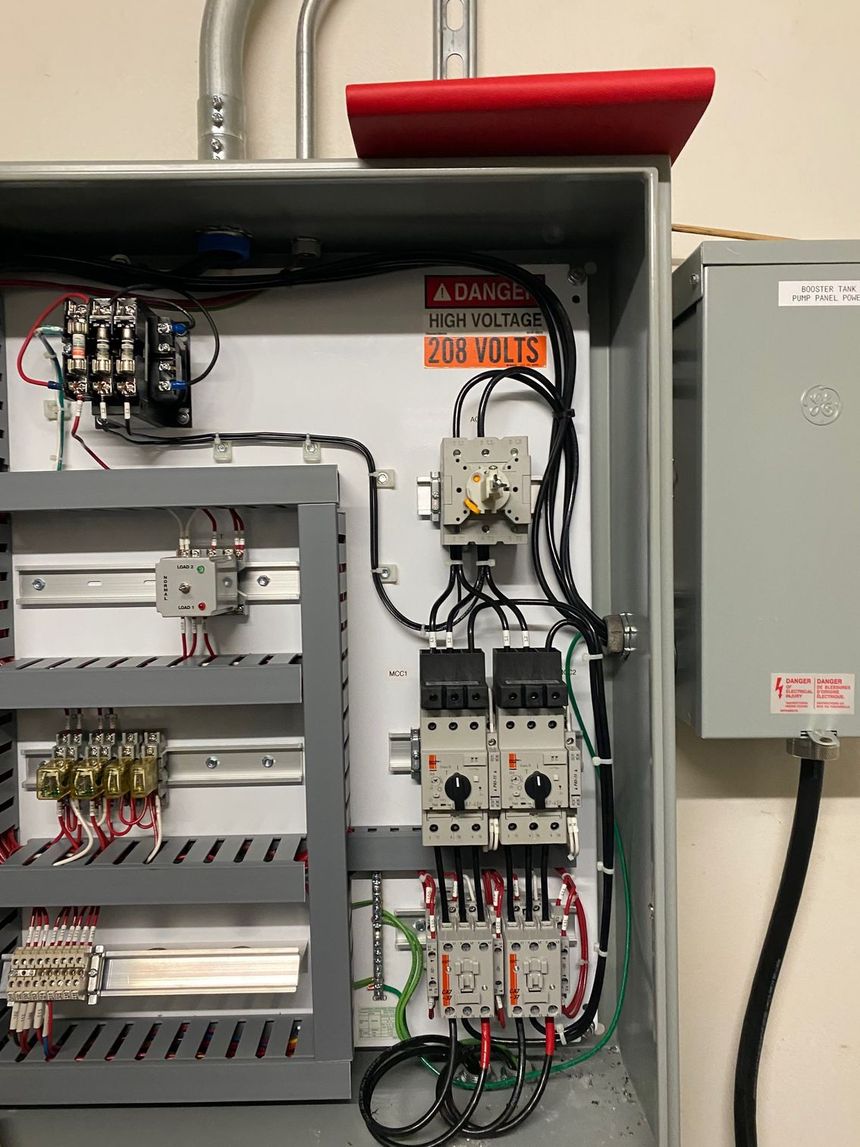Wall-mounted electrical control panel with tangled wiring, switches, and meters in a utility room