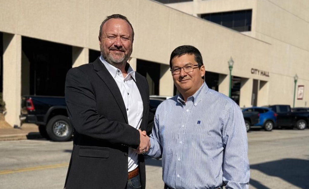 Two men shaking hands in front of a City Hall building.