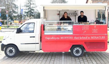 Un furgone rosso adibito a food truck è parcheggiato all'esterno, con due persone che servono i clienti da un bancone rosso e bianco.