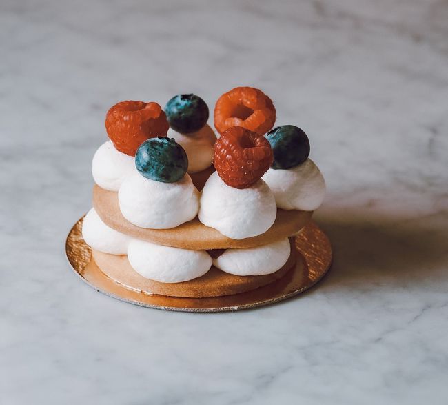 Mini dessert alla crema con frutta su base dorata, con ciuffi bianchi e frutti di bosco arancioni e scuri su una superficie marmorizzata.