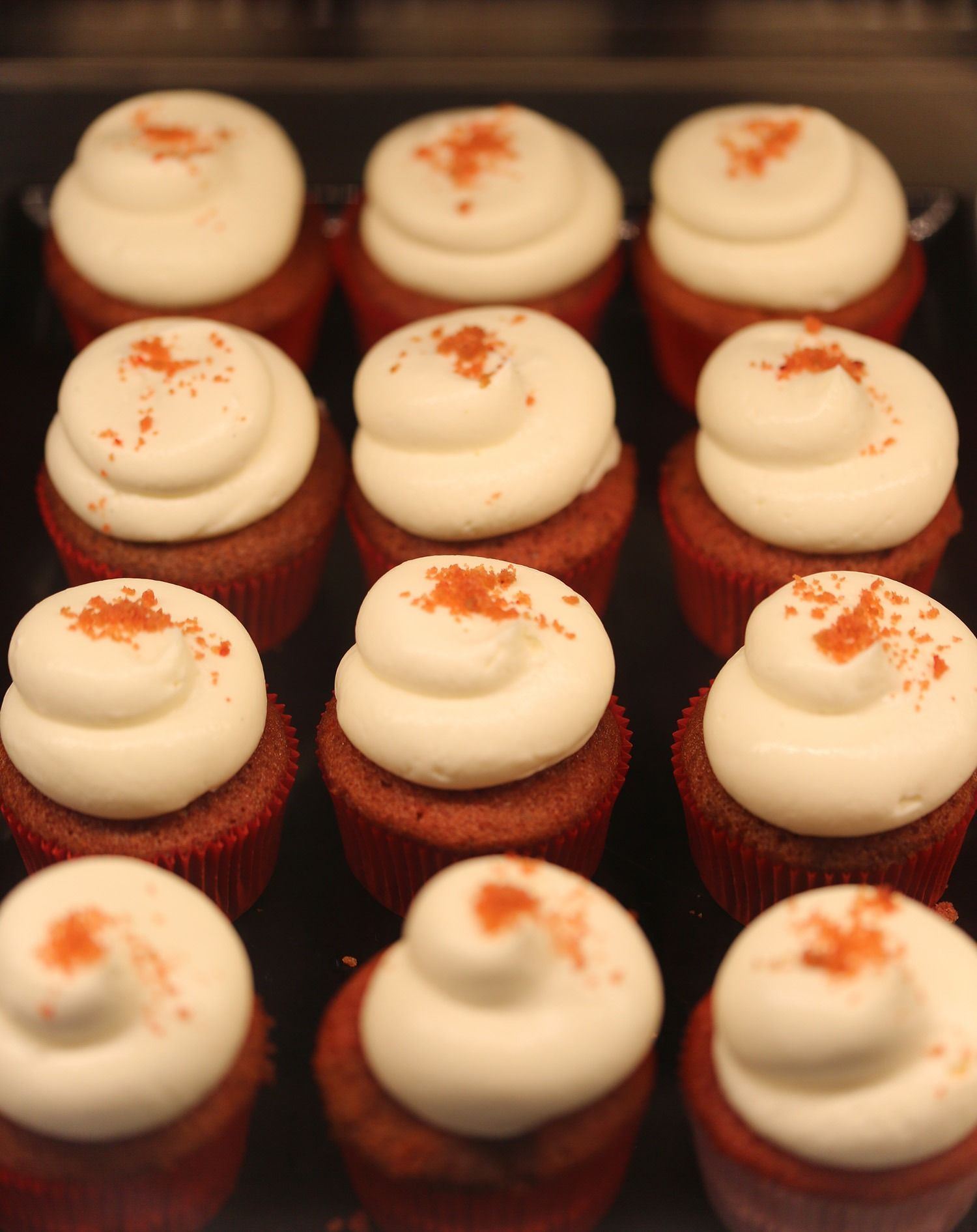 Cupcake di velluto rosso ricoperti di glassa bianca e cosparsi di cannella, disposti in file.