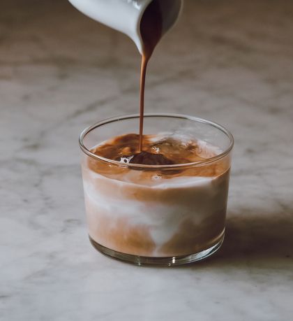 Il caffè viene versato in un bicchiere di latte macchiato freddo su un tavolo di marmo.