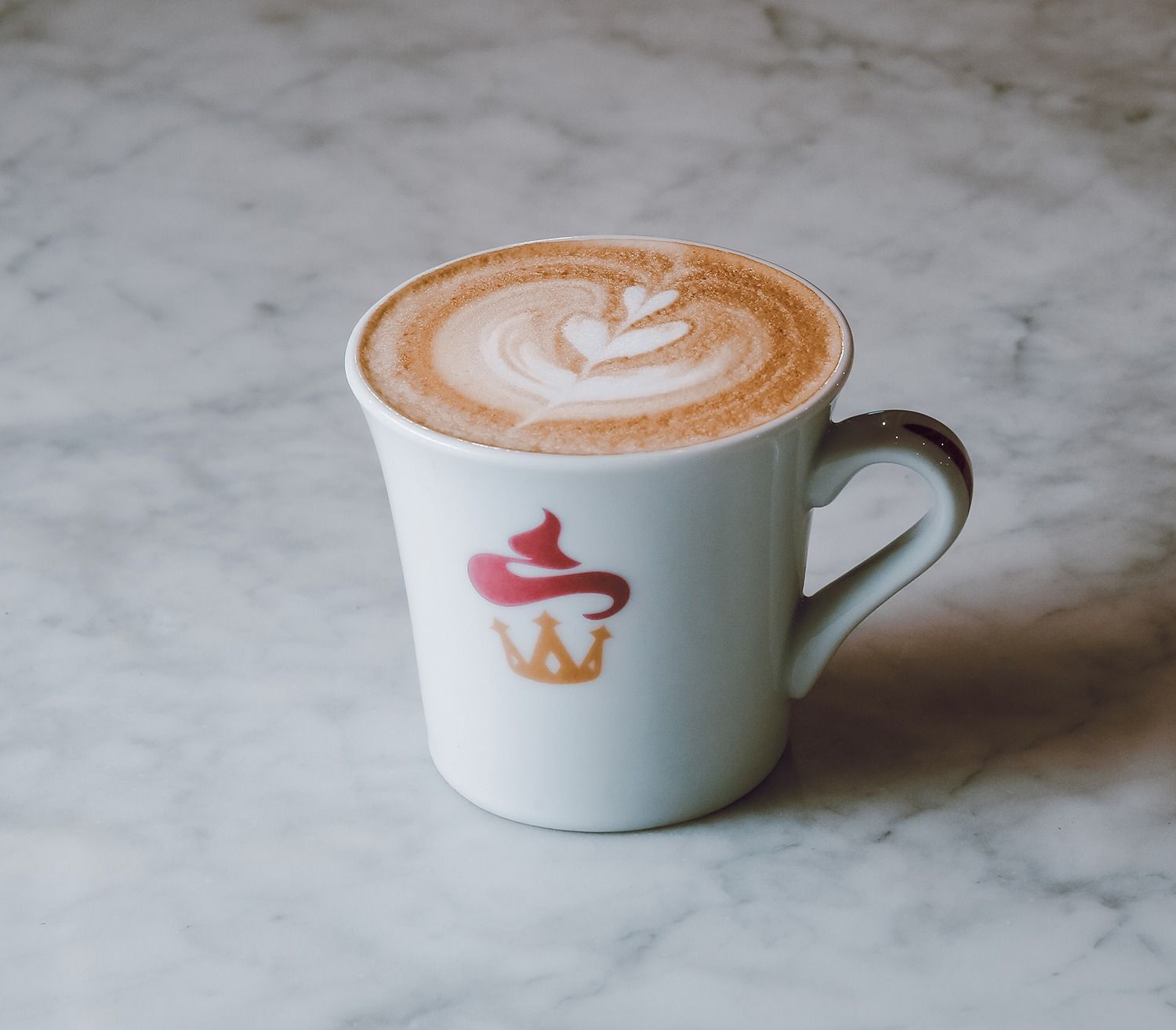 Tazza bianca da latte macchiato con decorazione di schiuma a forma di cuore su una superficie di marmo.