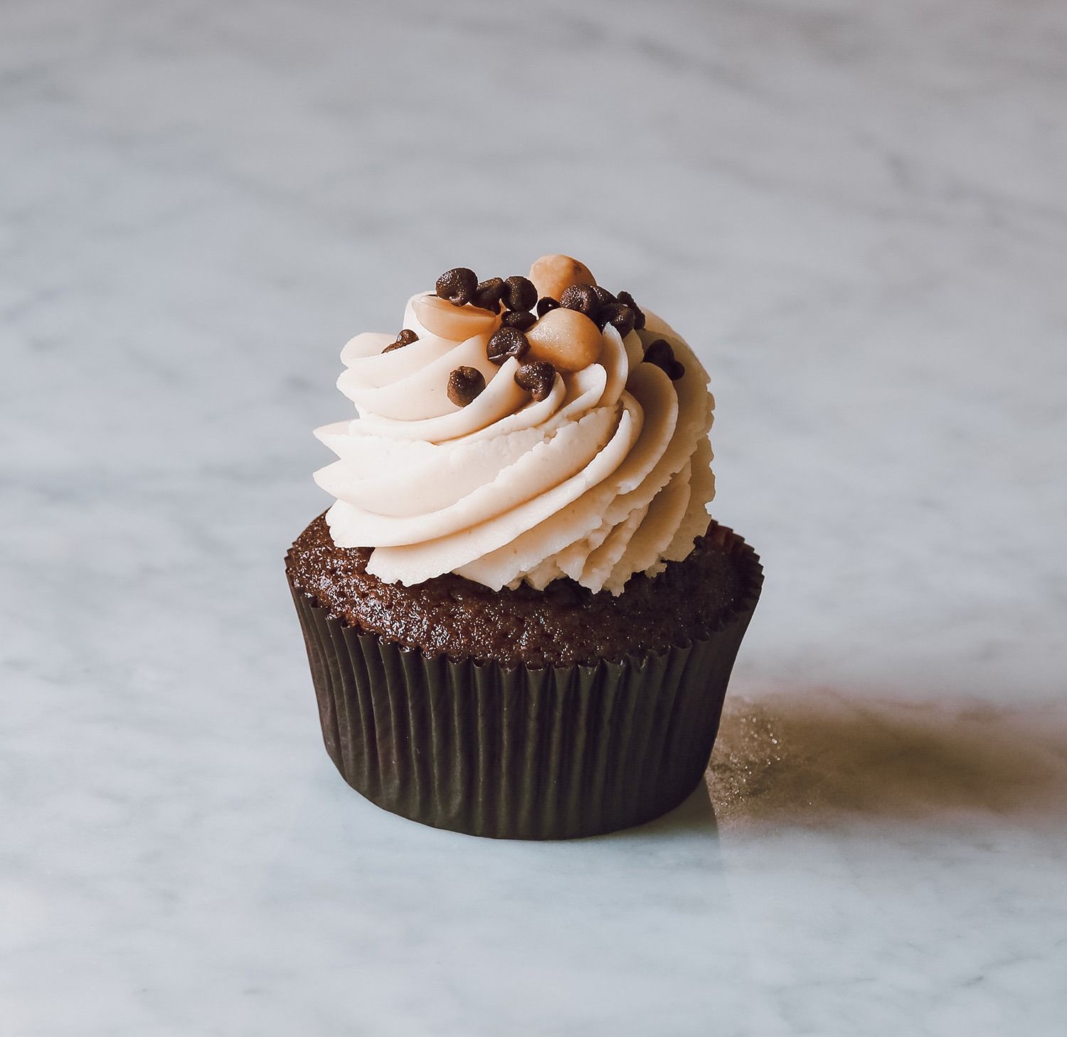 Cupcake al cioccolato con glassa alla vaniglia a spirale e granella di cioccolato su una leggera superficie marmorizzata.