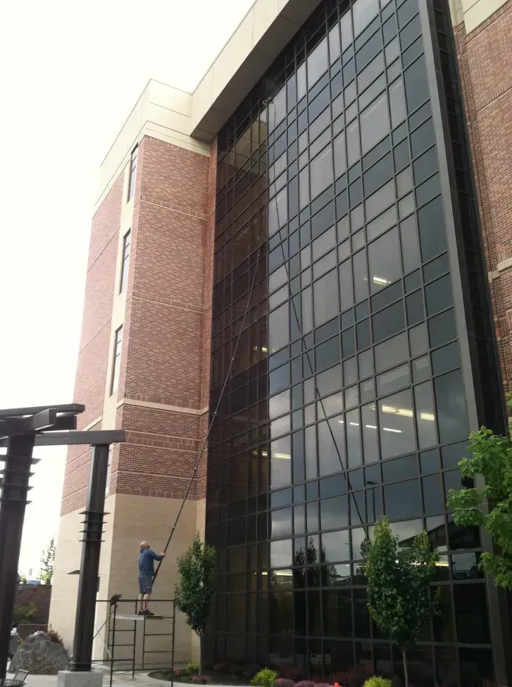Man on a ladder cleaning windows of a tall brick and glass building.