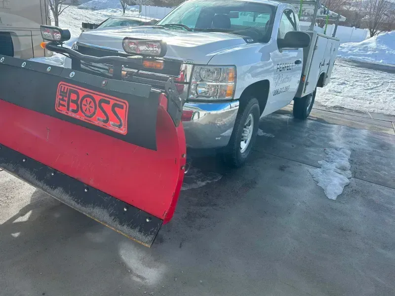 Silver pickup truck with red snowplow, parked on ice.