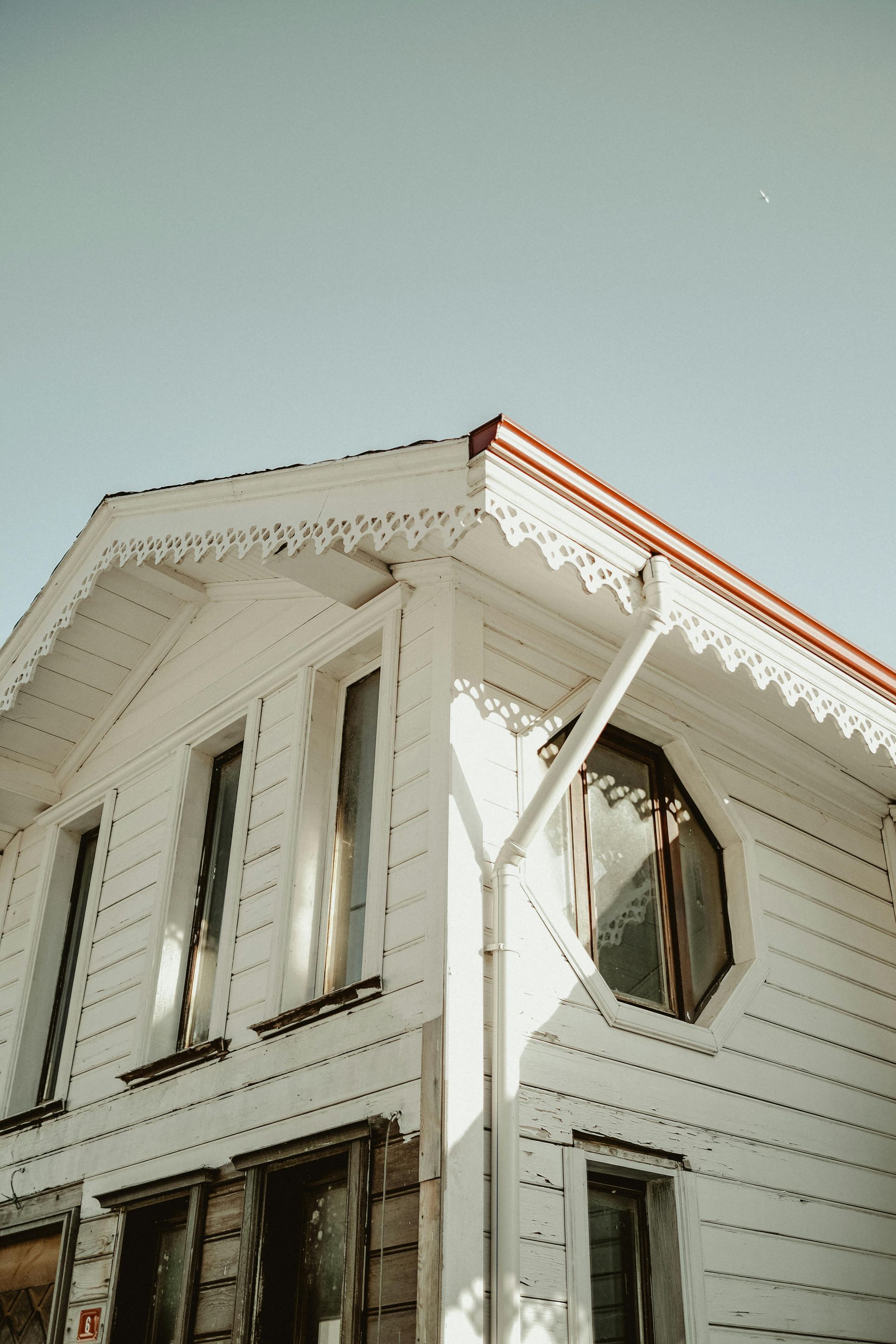 White, wooden house with decorative trim and red roof under a pale blue sky.