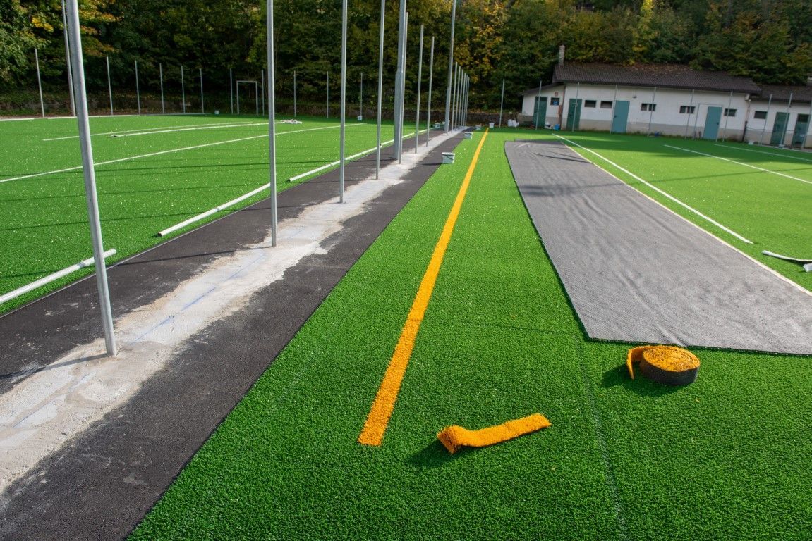 Artificial turf sports field under construction, with yellow line, concrete, and equipment.