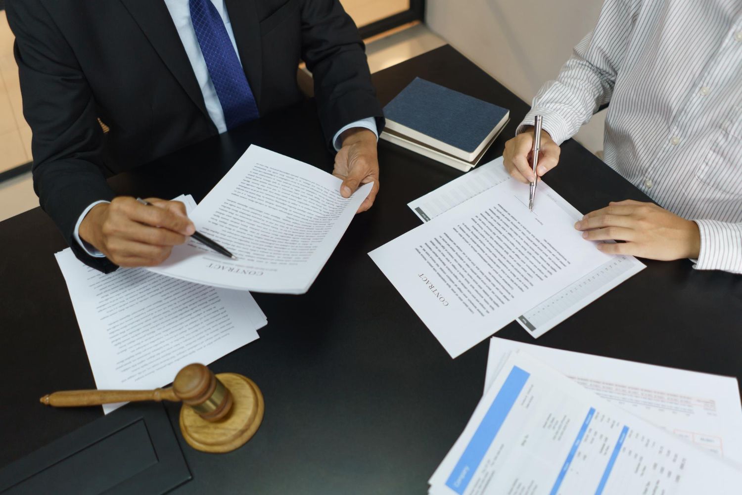 Two professionals in formal attire reviewing legal documents at a desk with a wooden gavel.