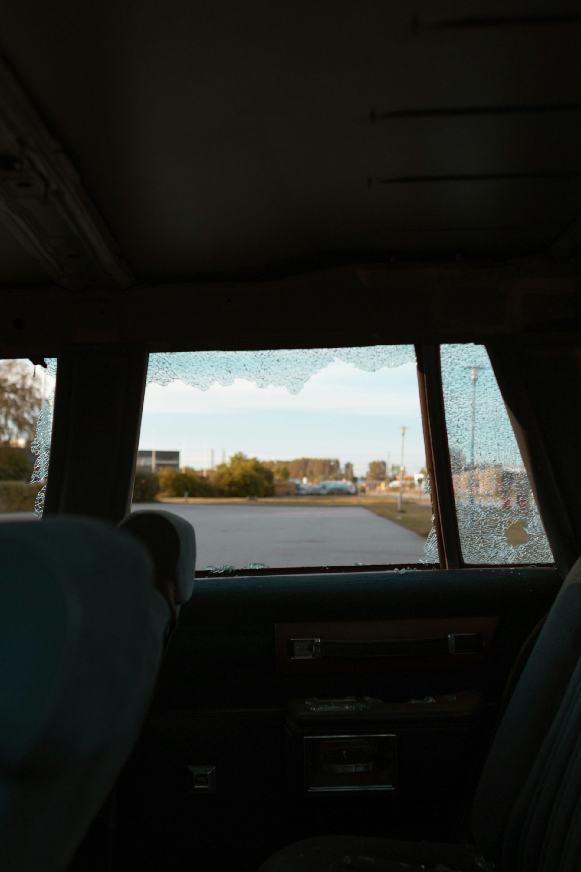 A view from inside a car looking out a back window that has been shattered, revealing an outdoor scene of a parking lot.
