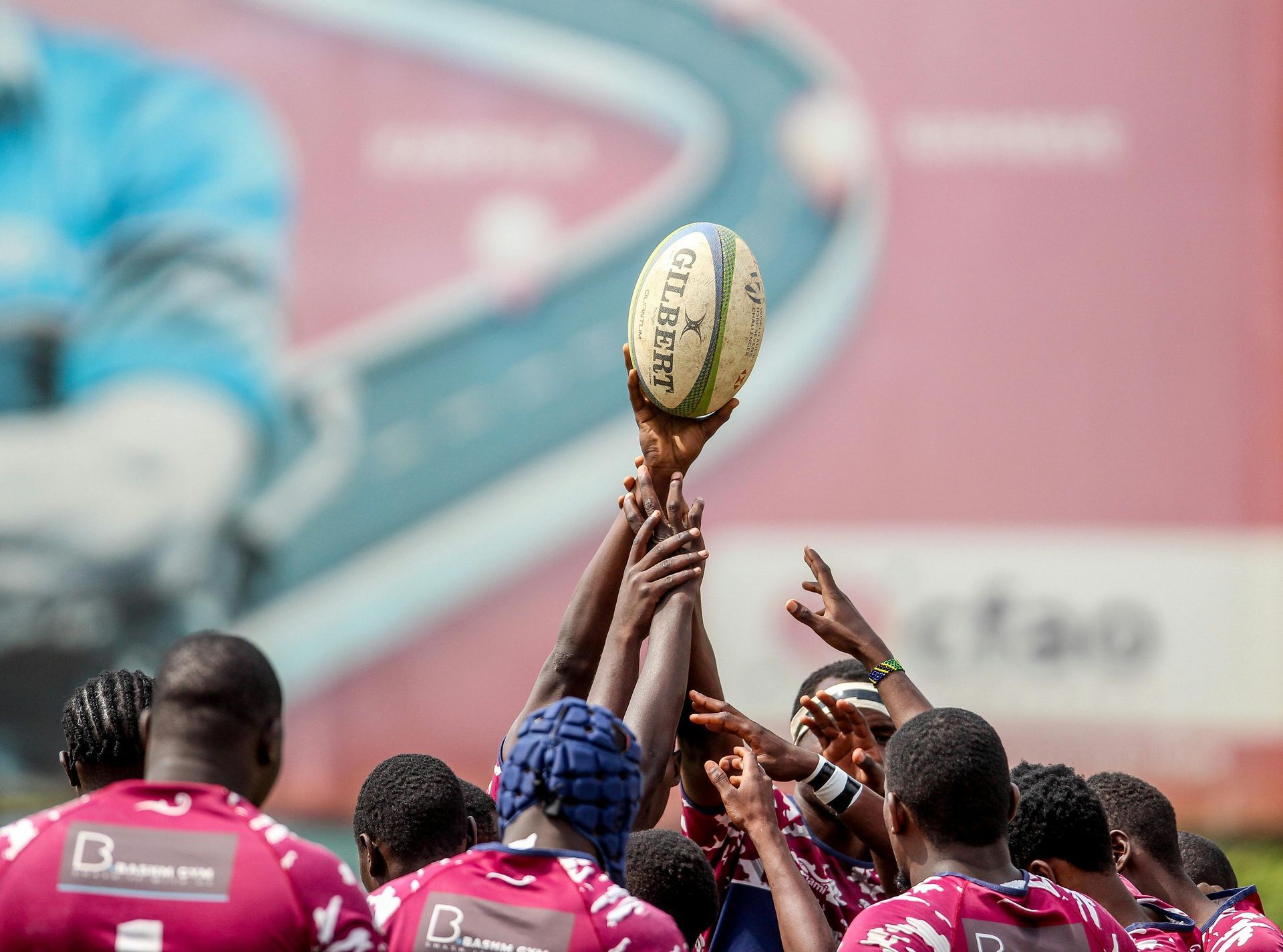 A group of rugby players in maroon jerseys reaching up to catch a ball during a line-out on a field.