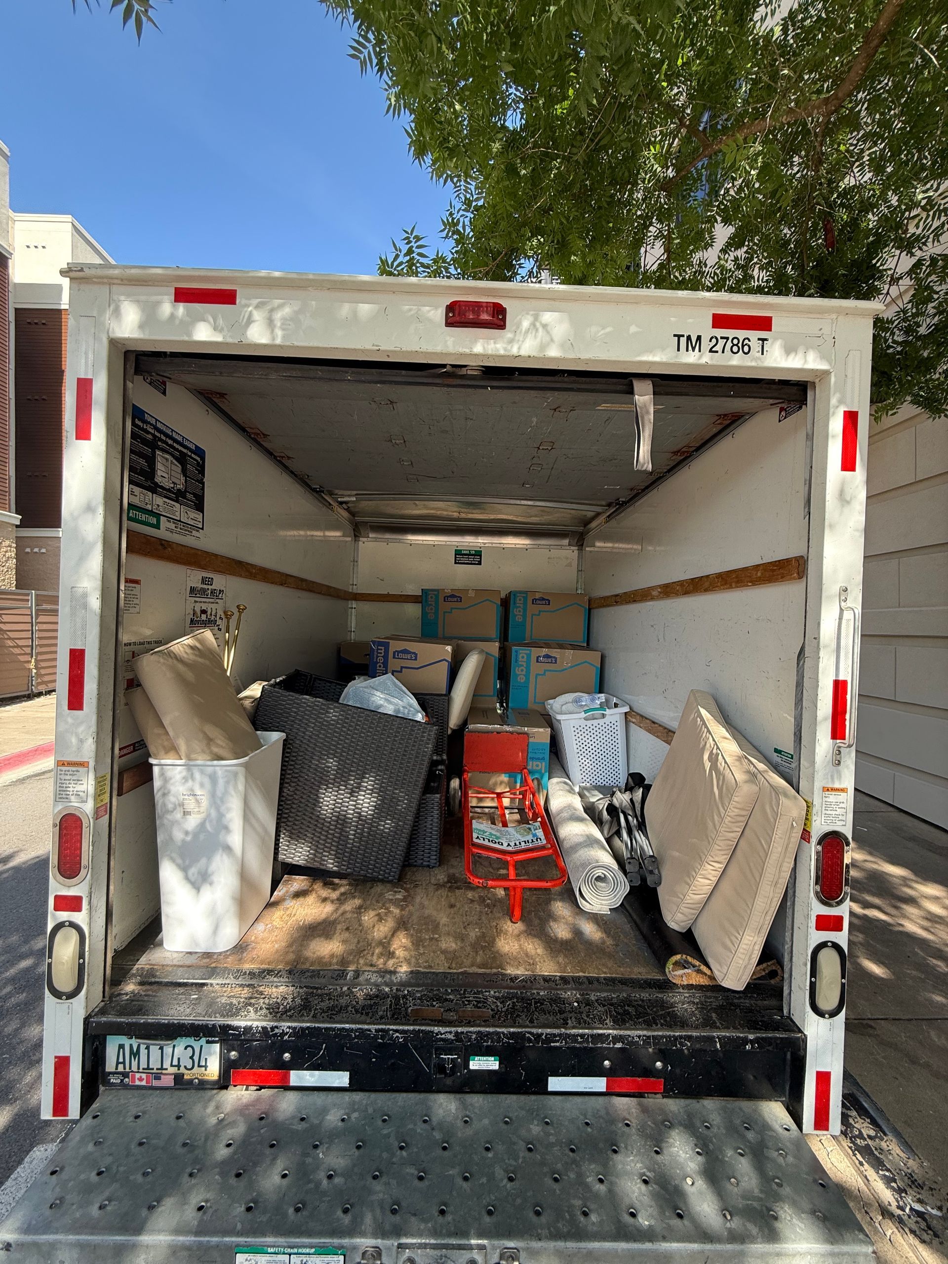 Back of a moving truck filled with furniture and boxes, outdoors in a sunny setting.