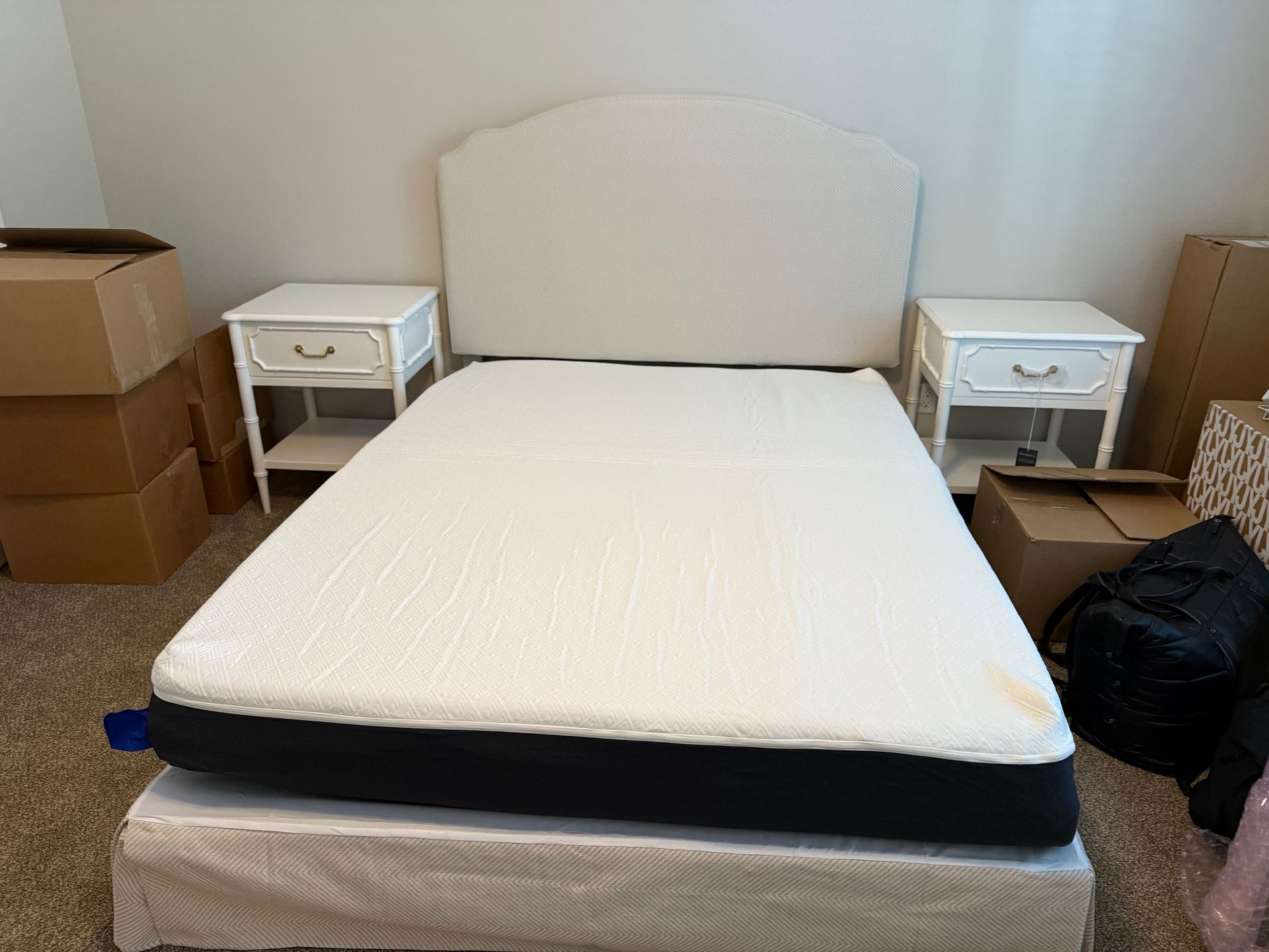 Bed with white headboard and nightstands, boxes in the background.