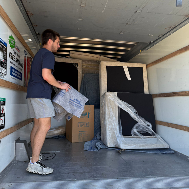 A man loading furniture into a moving truck. He holds a protective pad.