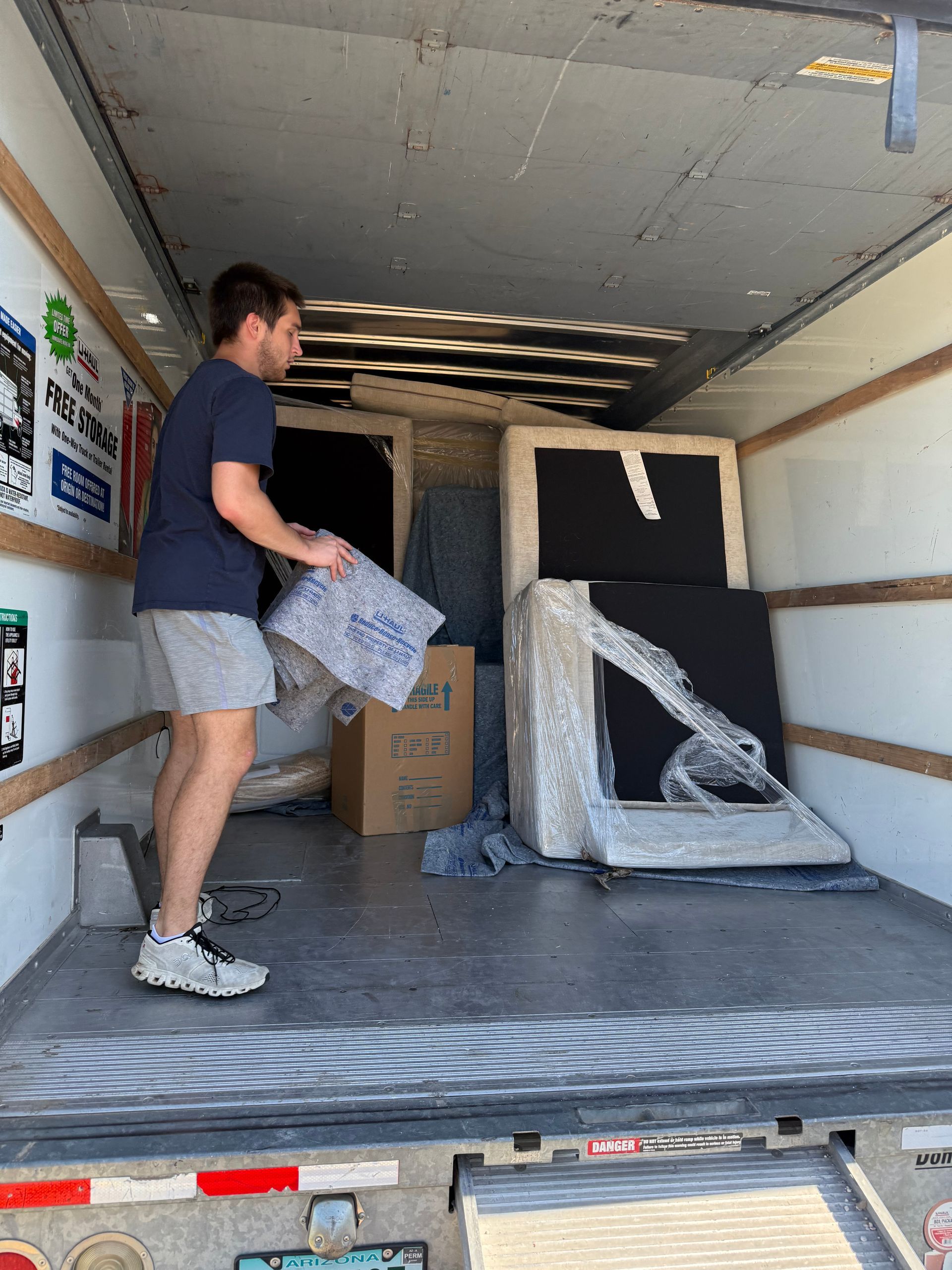 Man loading a moving truck with furniture. He carries paper, boxes, and wrapped items.