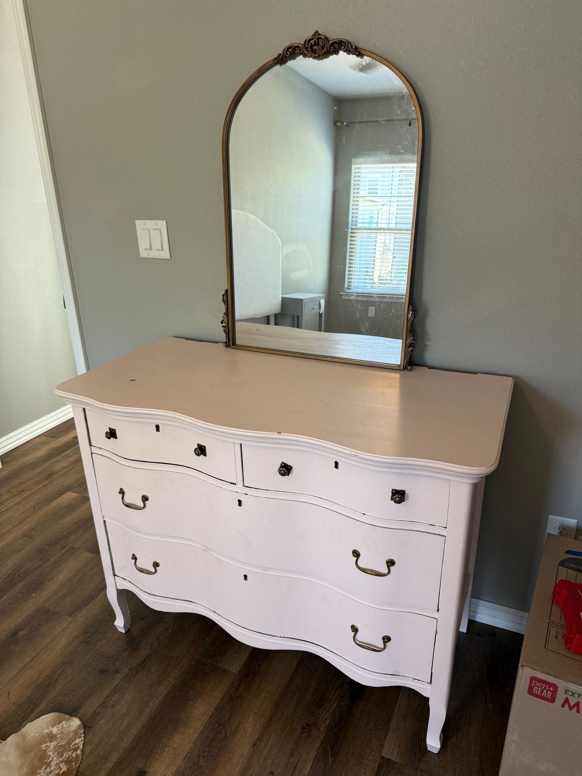 Pink dresser with mirror against a gray wall. Brown floors.